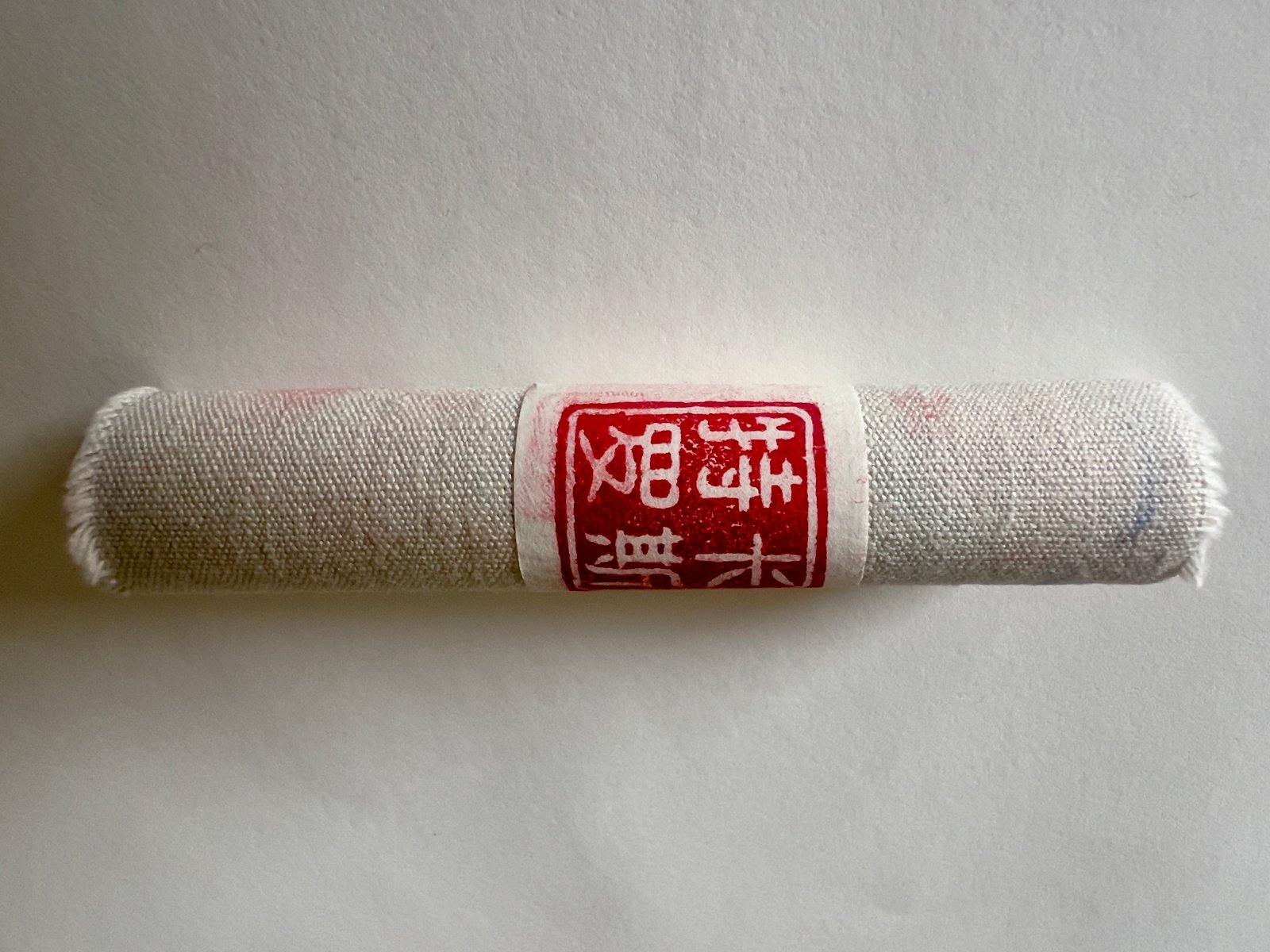 The book rolled — cotton strip bound by a rice paper ring stamped with the studio chop